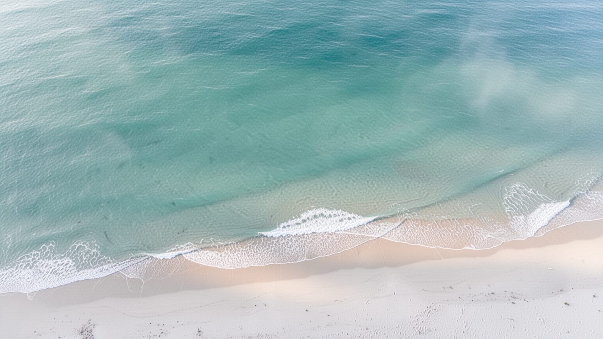 Calm turquoise sea meeting a pale sand shore from above